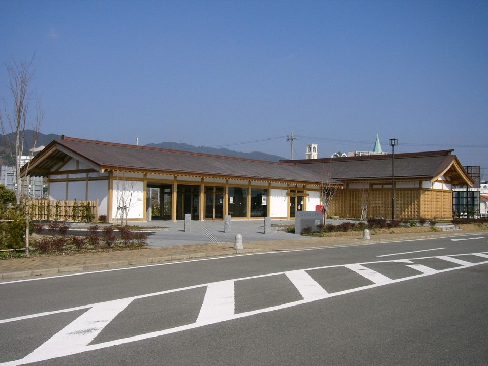 舗装された道路の先に白い壁と木の温もりを感じさせる柱を持つ伝統的な和風建築の意匠を取り入れた平屋建ての近代的な施設の外観写真