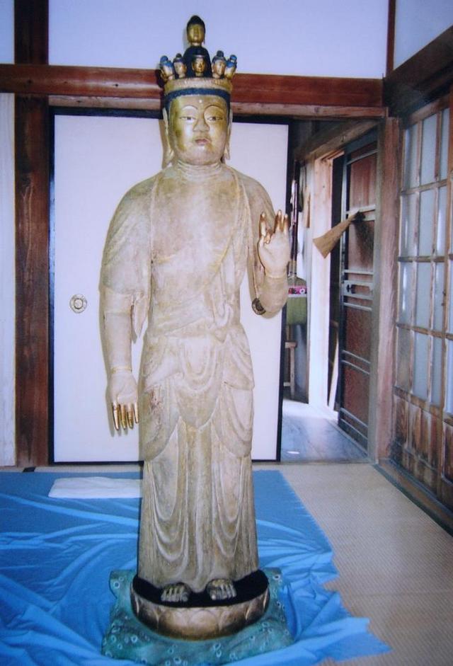 装飾冠を戴く立像が流麗な衣文をまとい、片手を上げて静かに佇み畳敷きの室内に安置された様子を捉えた写真