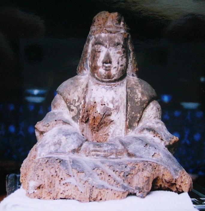 素朴な木彫の像が細やかな衣文の襞をまとい胡坐で座っており静かな佇まいを捉えた写真