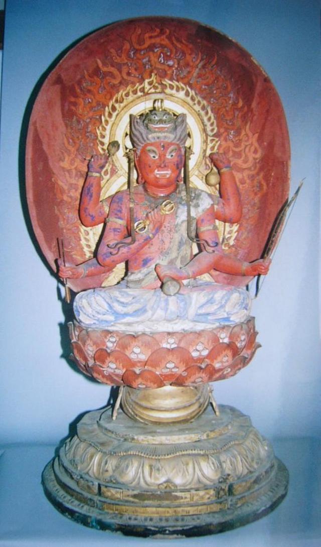赤い顔と複数の腕を持つ仏像が炎に包まれた大きな光背を背負い、細かな装飾の蓮華座に端然と坐して威厳を示す写真