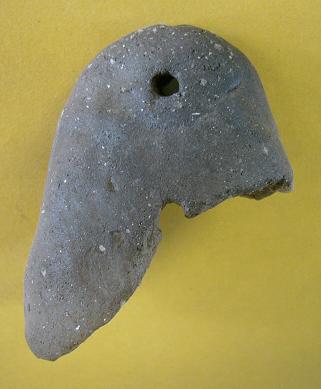 黄土色の背景に置かれた穴の開いた不定形の風化石片が大きな欠損部と細かな粒状感を伴う表面の荒れを際立たせている写真
