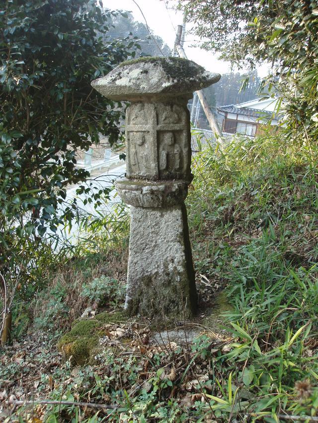 木々に囲まれた斜面に苔むした石灯籠が佇み、刻まれた面影や風化した質感が草木と調和して静かな景観をつくる写真