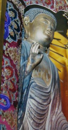 金色の光を背景に木彫の仏像が細かな衣文表現と落ち着いた印相を示し周囲の華やかな装飾とともに荘厳な存在感を放つ写真