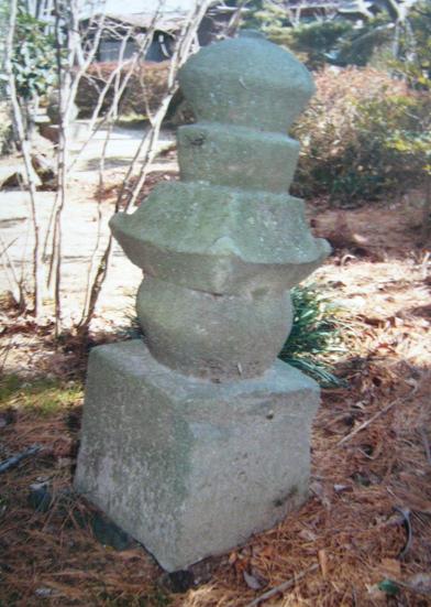 庭の落ち葉が積もる一角に苔むした石の多層塔が静かに佇み、風化した質感と重厚な形が長い歳月を物語る写真