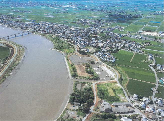 広大な平野を流れる大きな川と、その川岸に広がる集落や整然と区画された田畑を上空から俯瞰し、遠方の地平線まで続くのどかな田園風景と川に架かる橋を捉えた航空写真
