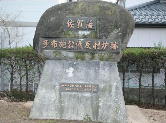 コンクリート製の台座の上に大きな自然石が載せられ、石の表面に「佐賀藩」「多布施公儀反射炉跡」という文字が刻まれたプレートが埋め込まれている石碑を正面から捉えた写真