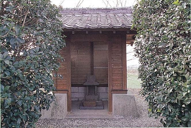 瓦屋根の付いた木造の小さなお堂のような建物の中に、石造りの祠が安置されており、その建物の両脇を背の高い緑の生垣が囲むようにして立っている、此荷大明神(このにだいみょうじん)の写真