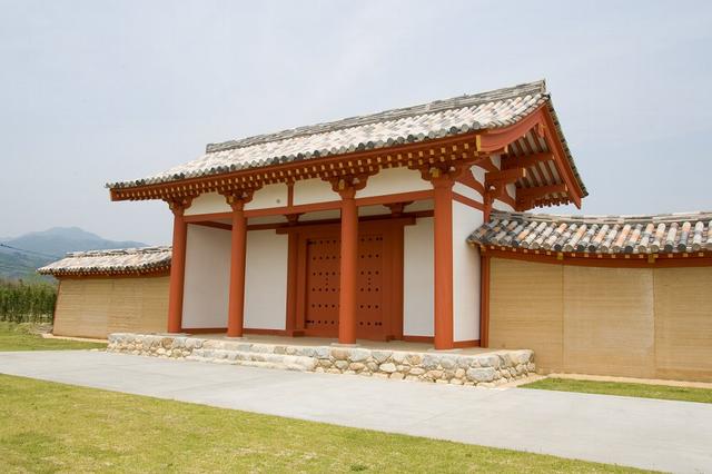 白い壁に鮮やかな朱色の柱が映える伝統的な瓦屋根の大きな門が、石積みの土台の上に堂々と構えられ、左右に土塀が続く肥前国庁跡の外観写真
