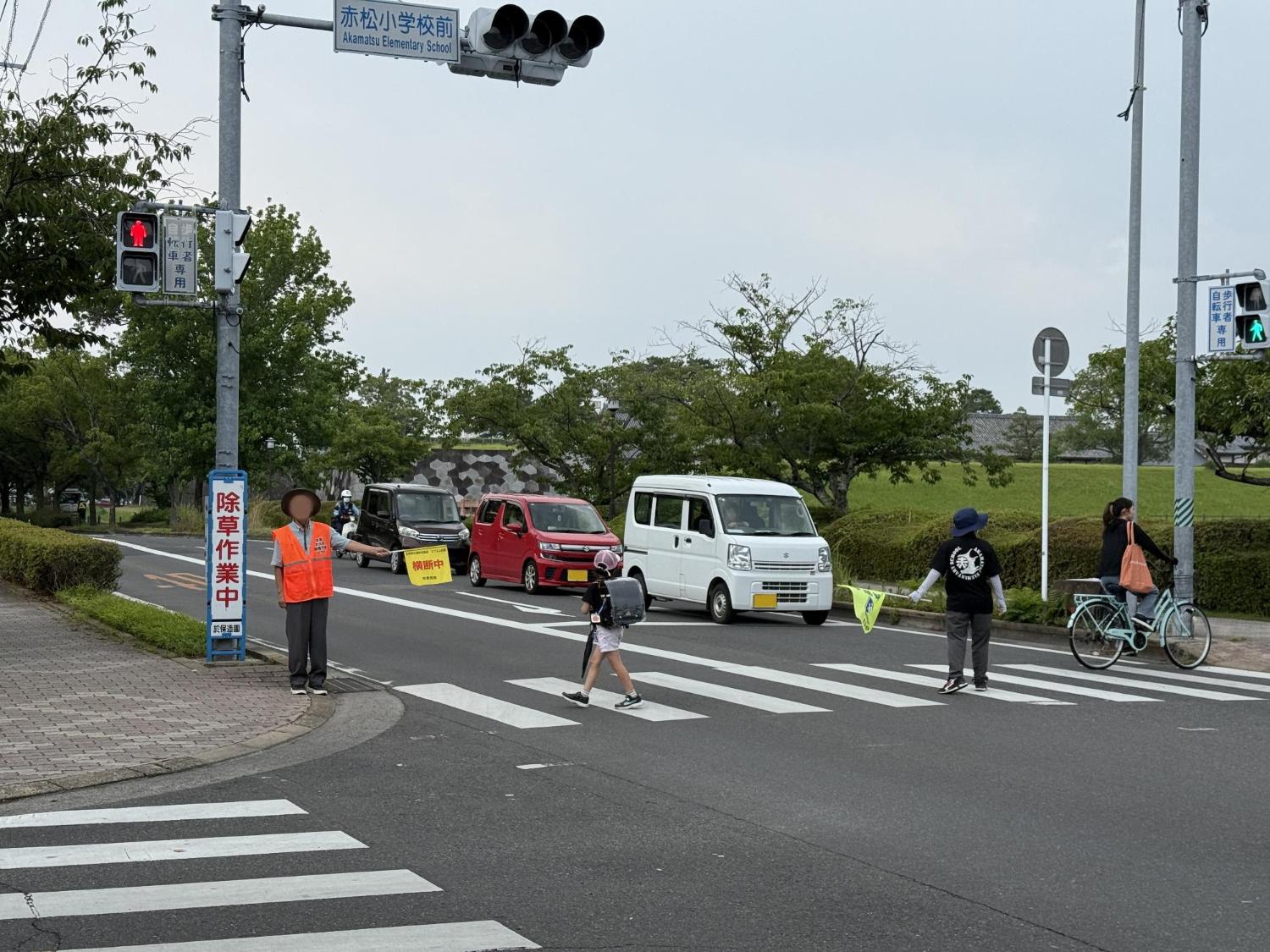 交通指導員が横断旗をもって、小学生が横断歩道を安全に渡れるよう誘導している。
