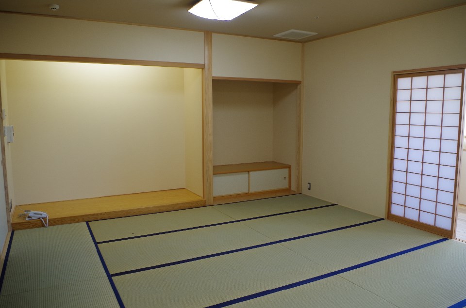 薄いベージュの壁と畳が敷かれた室内に、床の間や障子戸が整然と配置され落ち着いた雰囲気を漂わせる和室の写真
