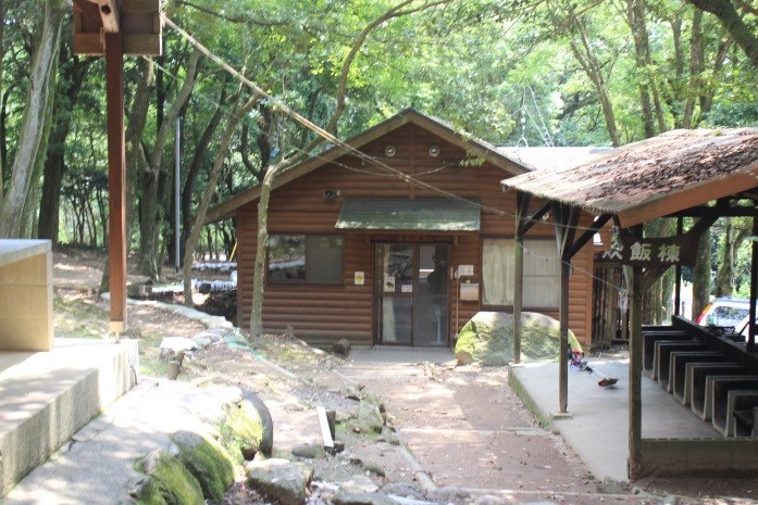 木々に囲まれた林間に木造の小屋と屋根付き炊事場が並び静かな自然の中の施設を捉えた写真