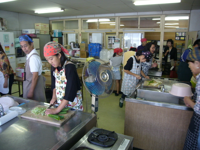 調理実習室で参加者たちがエプロン姿で野菜を刻んだり調理台で作業したりする様子を捉えた写真