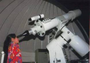 大きな白い天体望遠鏡を人物がのぞき込む様子がドーム形の観測室内で写された写真