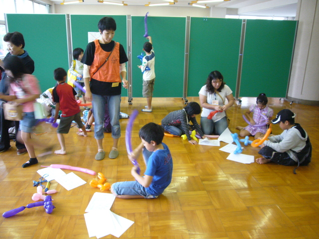 広い室内で子どもたちが色とりどりのペンシルバルーンを使って遊んだり作品づくりに励む活気ある様子の写真